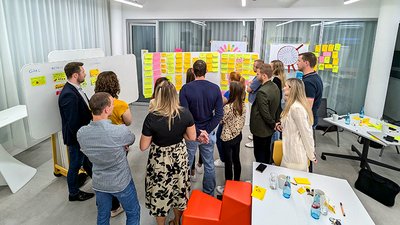Personengruppe beim Workshop blickt auf Whiteboards mit Postits