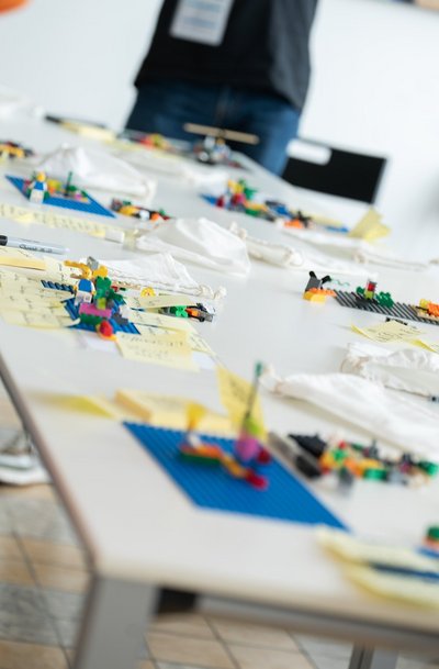 Lego Serious Play Workshop Tisch: Ein länglicher Tisch mit vielen kleinen Lego-Modellen und Notizzetteln von Workshop-Teilnehmern.