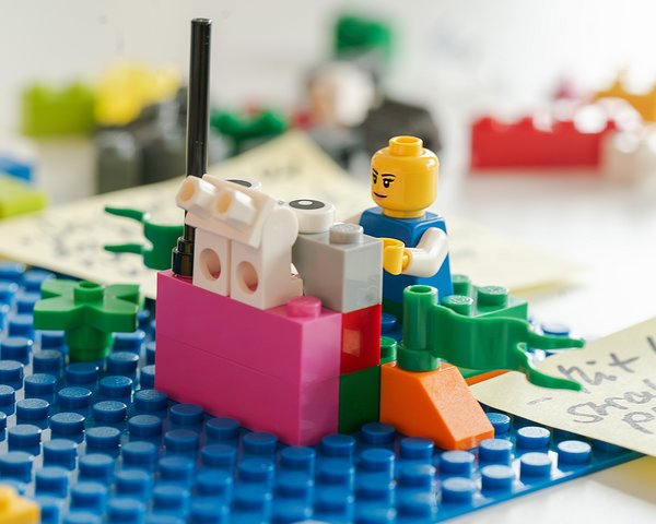 Lego Workshop: Nahaufnahme einer Lego-Figur und eines Modells mit Notizzetteln im Hintergrund.