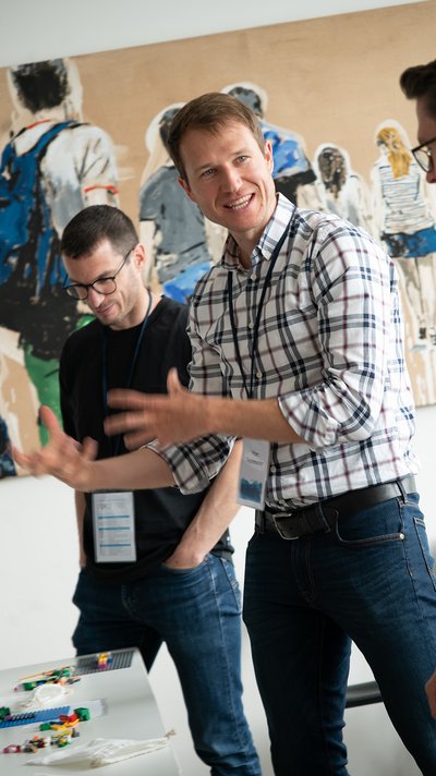 Lego Serious Play Workshop Teilnehmer: Zwei Teilnehmer diskutieren angeregt während eines Workshops mit Lego Bausteinen auf einem Tisch.