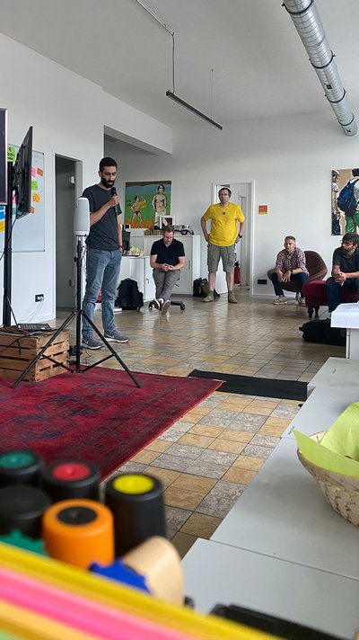 Jonathan Kaiser stellt dem Team sein Filmprojekt vor, im Hintergrund ein Monitor